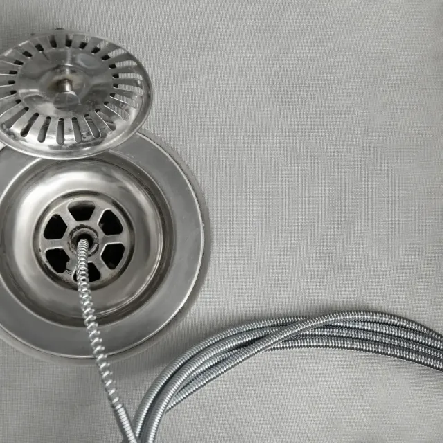 Stainless steel sink drain and strainer with braided hose on a light textured surface