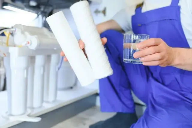 Plumber holding filter cartridges and a glass of clean drinking water beside an under-sink reverse osmosis system in Mesa, AZ Plumber holding filter cartridges and a glass of clean drinking water beside an under-sink reverse osmosis system in Mesa, AZ
